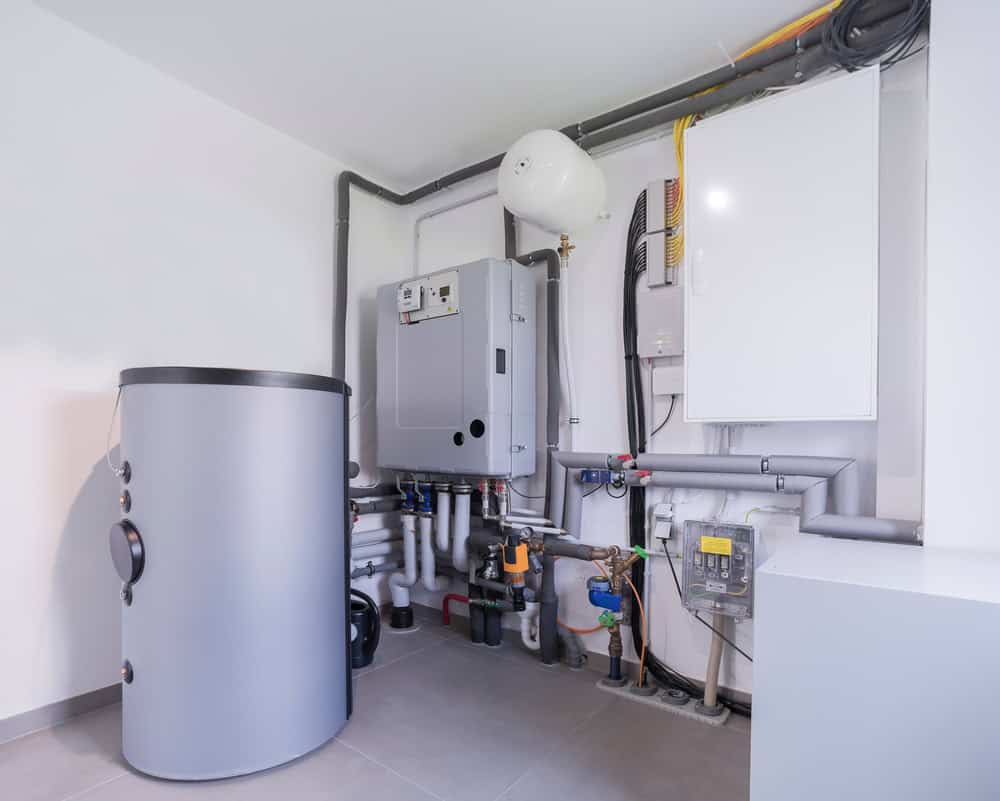 A clean, modern boiler room with various pieces of heating and plumbing equipment. The room features a large cylindrical water tank, pipes, valves, and a wall-mounted control unit. The setup is organized and well-maintained, indicating efficient systems in place for seamless boiler maintenance.
